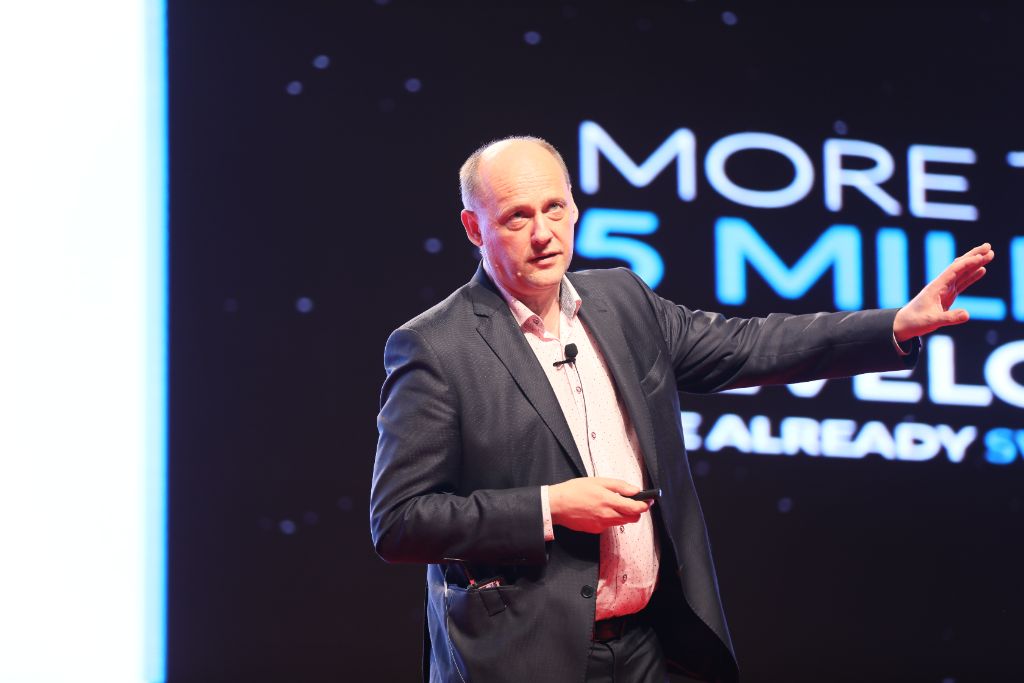 Speaker presenting on stage with data visuals